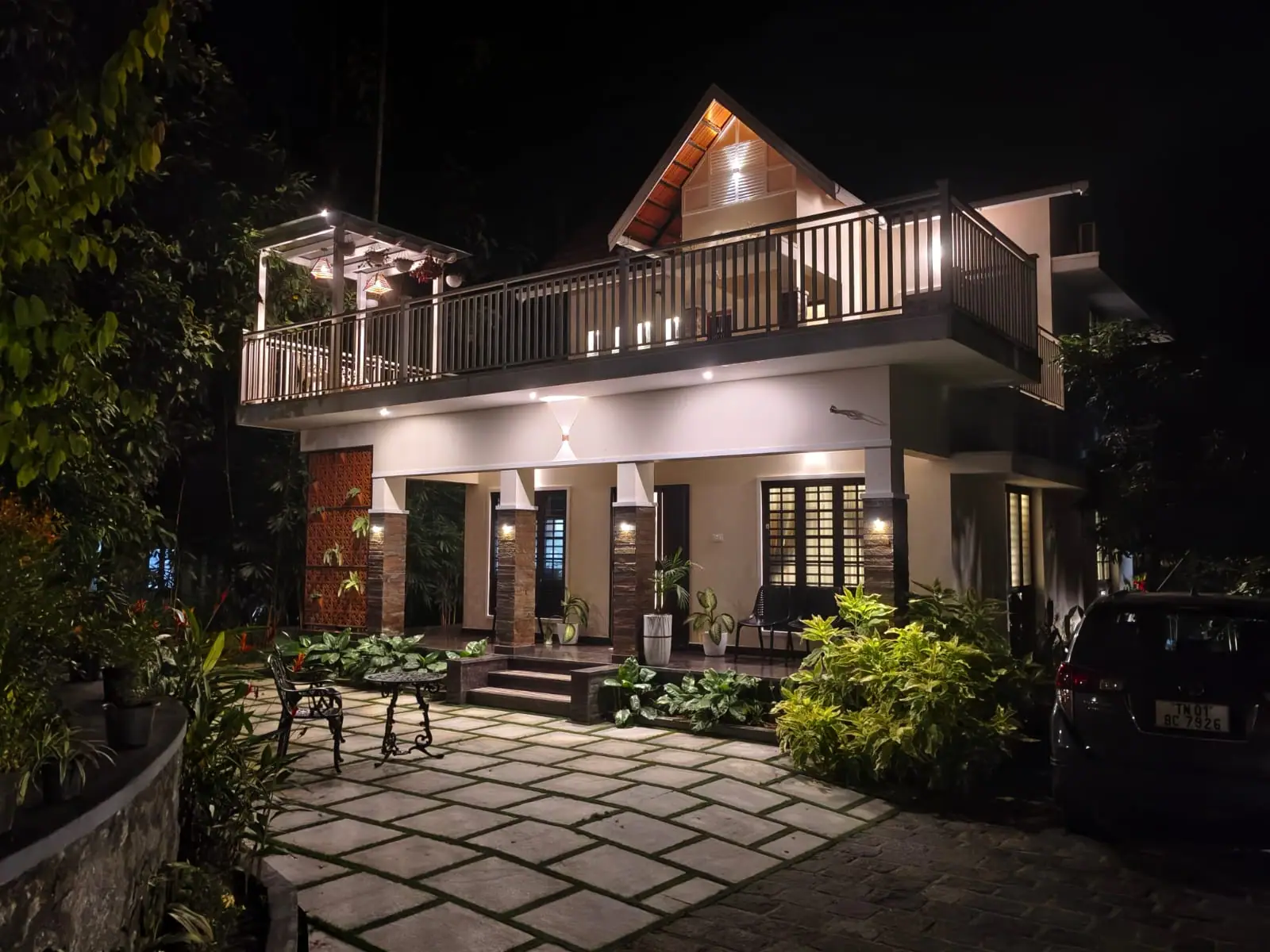 Nyra Thottam villa lit warmly in the evening, showing the stone-paved courtyard, veranda pillars and upper balcony